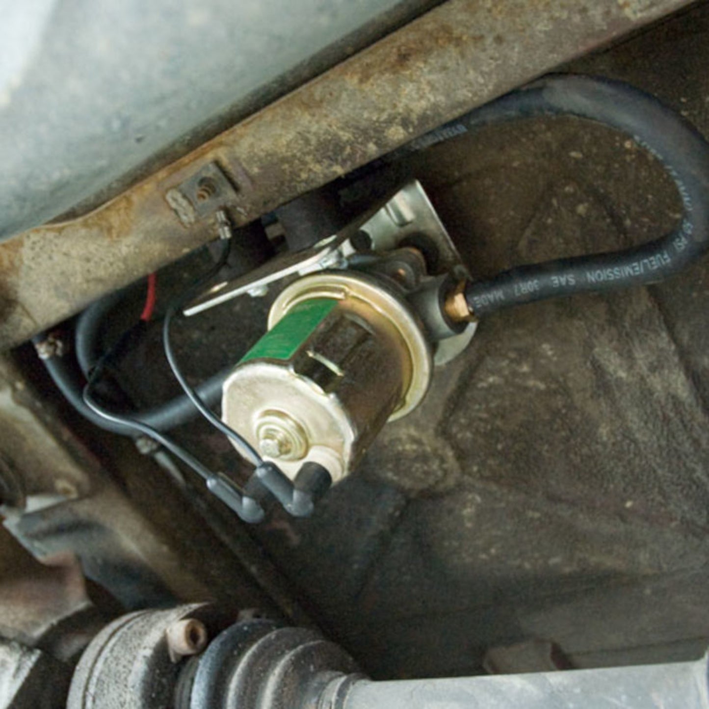 Carter 12V in-line fuel pump installed under vehicle: mounted with bracket, connected to fuel line and wiring for efficient auxiliary tank transfer.
