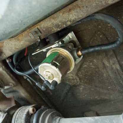 Carter 12V in-line fuel pump installed under vehicle: mounted with bracket, connected to fuel line and wiring for efficient auxiliary tank transfer.