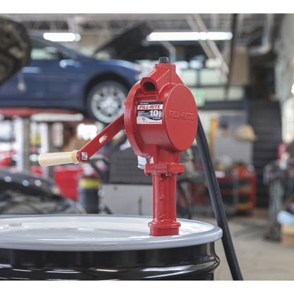 Fill-Rite FR112 rotary hand pump in garage, man transferring fuel from drum to jerry can with wooden handle and brass nozzle